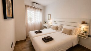 Ein Hotelzimmer mit zwei Betten, einem Nachttisch mit Lampe, einem kleinen Regal mit Teddybär und einem gerahmten Bild an der Wand.