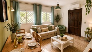 Ein gemütliches Wohnzimmer mit einer Couch, einem Esstisch, Stühlen und einem grünen Sessel, mit Holzboden.