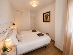 Ein Schlafzimmer mit Bett, Nachttischlampen, einer Topfpflanze, einem gerahmten Bild an der Wand und einem Kleiderschrank mit Schiebetüren.
