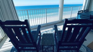 A balcony with two wooden chairs and a small table, overlooking a beach with a railing. - Tower 2, three bedroom! Great Views!! FREE BEACH CHAIRS! (Panama City Beach)
