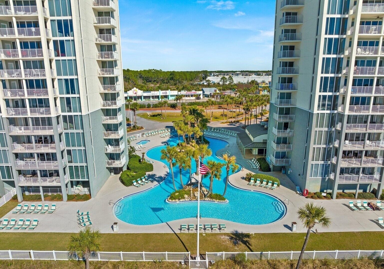 A high-rise hotel with multiple balconies, a central swimming pool, and a landscaped area with lounge chairs.