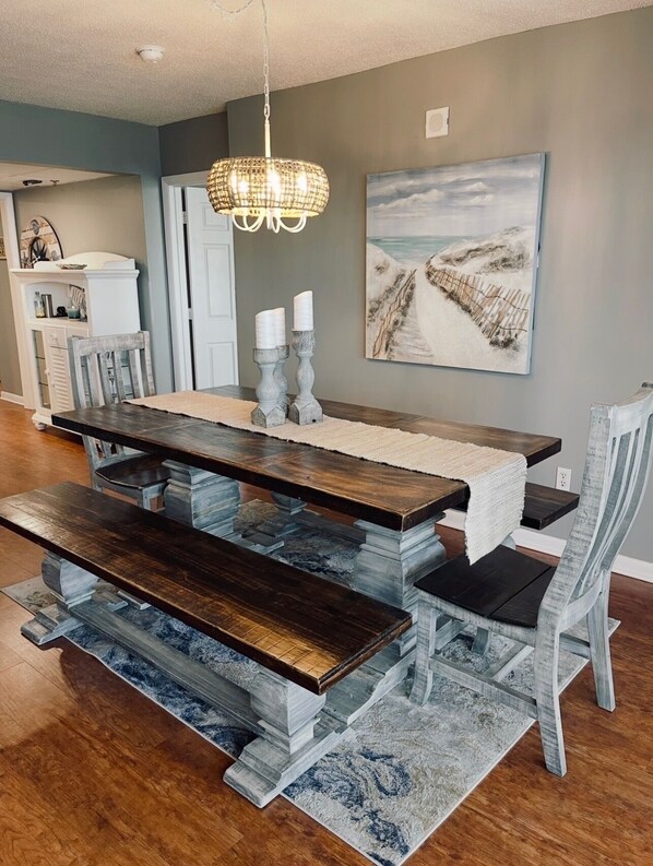 A dining area with a wooden table, benches, and a chandelier. - Tower 2, three bedroom! Great Views!! FREE BEACH CHAIRS! (Panama City Beach)