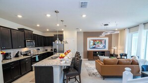 A modern kitchen with dark cabinets, a central island, and a dining area with a brown leather sofa.