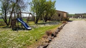 A rustic outdoor area with a wooden slide, a stone building, and a gravel path. - Corbezzolo (Asciano)