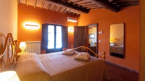A bedroom with a wooden bed, bedside tables, a mirror, and a radiator. - Corbezzolo (Asciano)