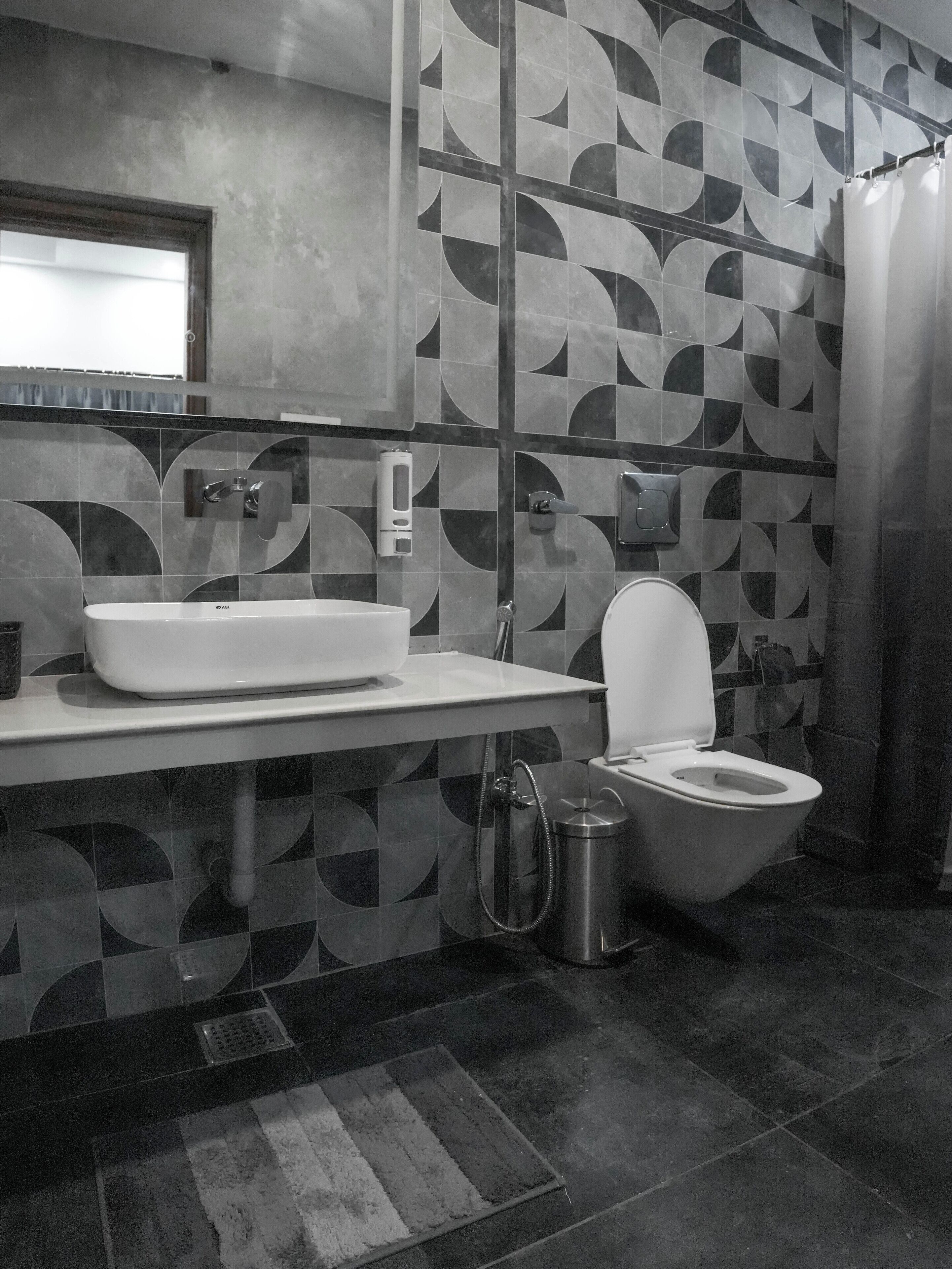 A modern bathroom with a geometric tile backsplash, a white sink, a toilet, and a shower curtain.