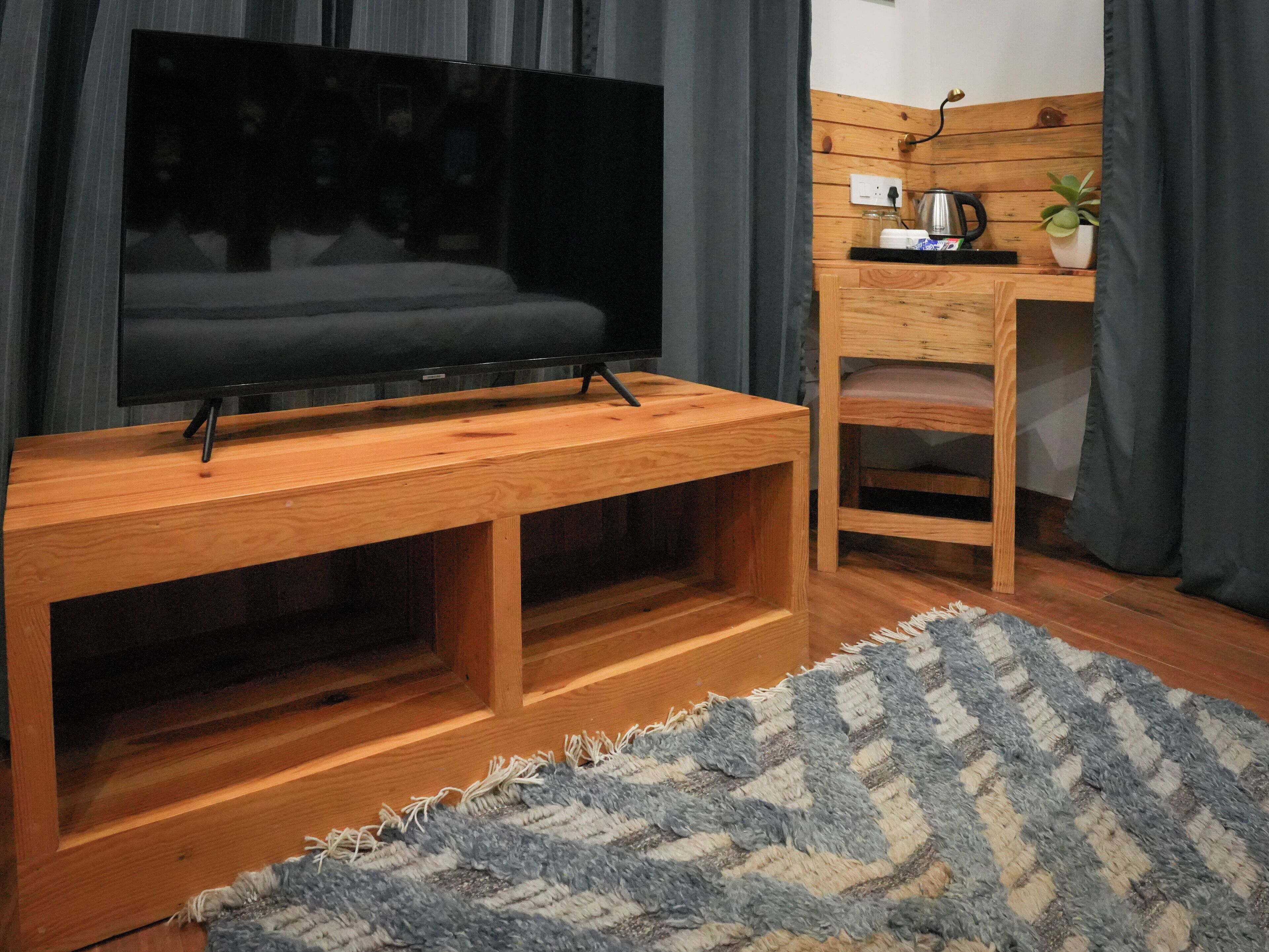 Un mueble de madera con un centro de entretenimiento, un televisor de pantalla plana, una pequeña mesa de madera con una tetera y una silla.