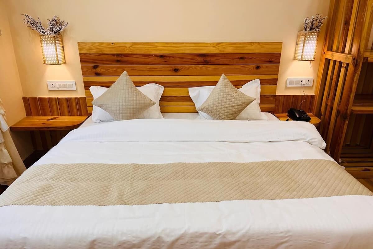 Uma cama bem arrumada com cabeceira de madeira, duas mesas de cabeceira com abajures e um luminário fixado na parede.
