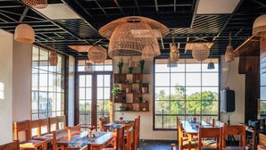 Un restaurante con mobiliario de madera, ventanas amplias e iluminación colgante de ratán.