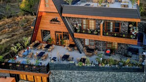 Un edificio de dos pisos con techo inclinado, fachada de madera y un patio con mobiliario exterior.