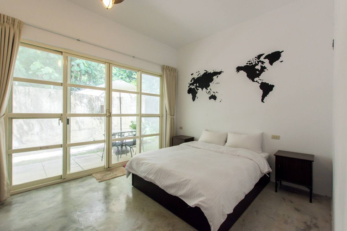 Un dormitorio con una cama grande, un mapa del mundo en la pared y un ventanal corredero que da a un espacio exterior.