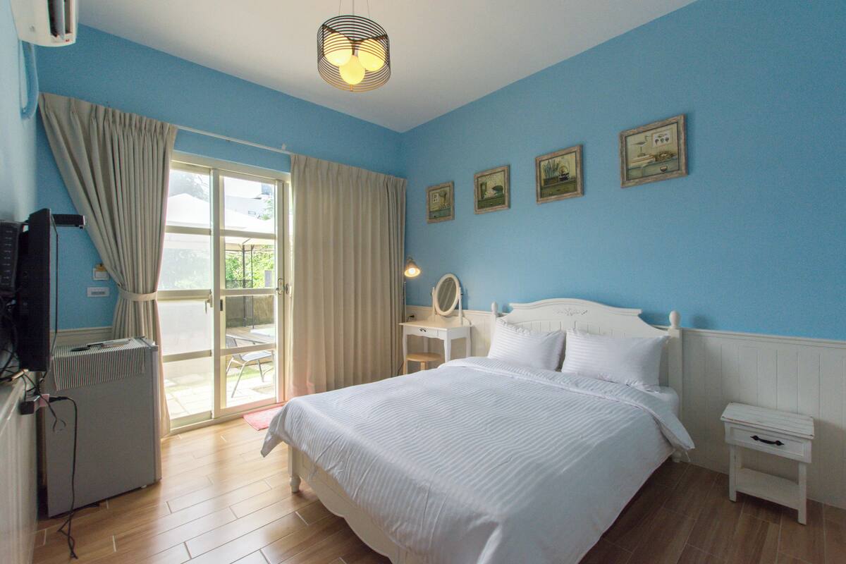 Un dormitorio con cama, mesita de noche, silla, ventana con cortinas y radiador.