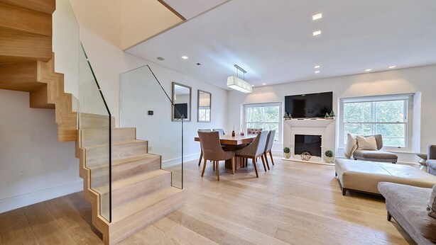 A spacious living area with a wooden staircase, a dining table with chairs, a sofa, and a fireplace. - Luxury 2 Bedroom Hyde Park Penthouse with Rooftop (London)