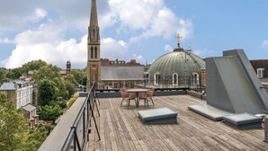 A rooftop terrace with a dining table and chairs, overlooking a cityscape with historic buildings and a church tower. - Luxury 2 Bedroom Hyde Park Penthouse with Rooftop (London)