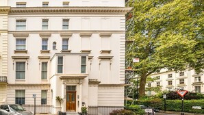 A white building with a classic architectural style, featuring a central entrance with a door and windows on the upper floors. - Luxury 2 Bedroom Hyde Park Penthouse with Rooftop (London)