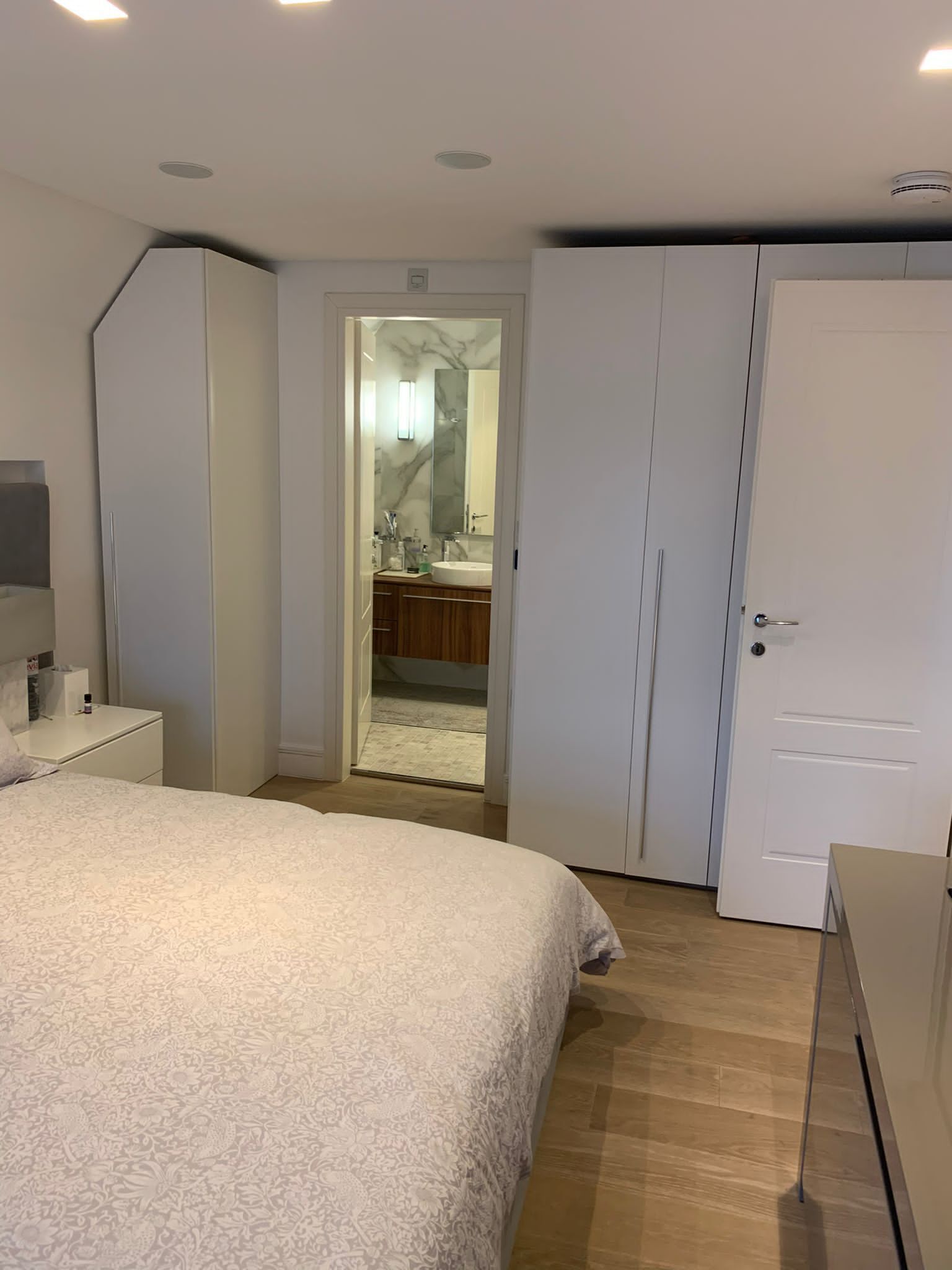 A bedroom with a large bed, a wardrobe, a nightstand, and a bathroom visible through an open door.