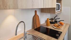 A modern kitchen with a sink, a wooden cutting board, a glass of orange juice, a frying pan, and a plate with croissants. - Quality Aparthotel Nancy Centre (Nancy)