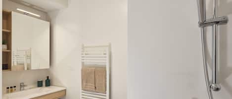 Un baño con tocador blanco, espejo, toallero y ducha con cabezal de ducha de mano.