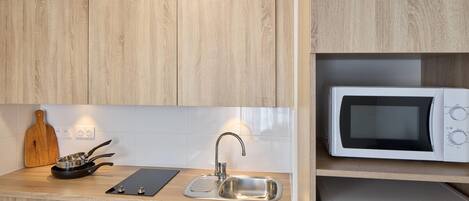 A kitchen with wooden cabinets, a stainless steel sink, a microwave, and a cutting board.