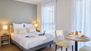 A hotel room with a neatly made bed, a dining table with breakfast items, and a laptop on the bed. - Quality Aparthotel Nancy Centre (Nancy)