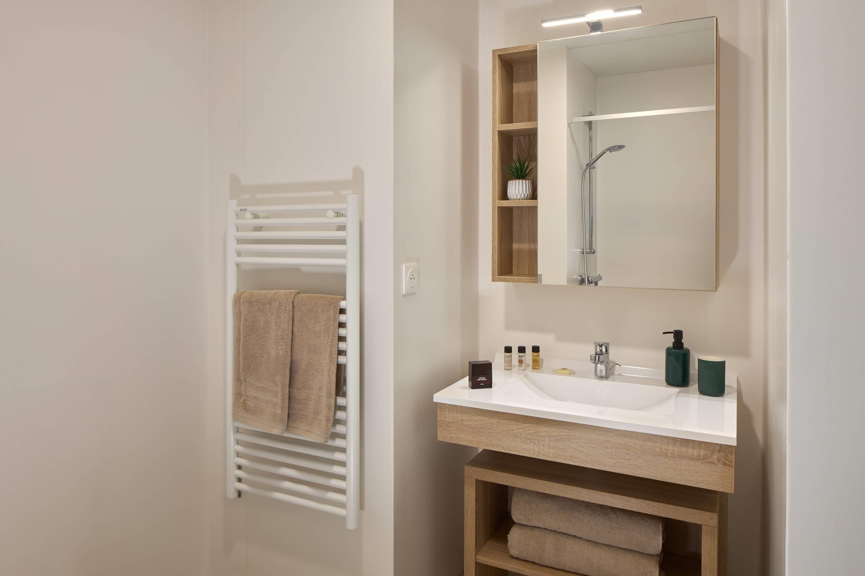 Une salle de bain moderne avec un lavabo blanc, un meuble-lavabo en bois et un porte-serviettes sur lequel est posée une serviette.