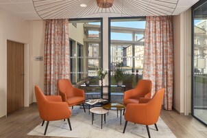 A modern room with two orange chairs, a small table, and large windows with floral curtains.