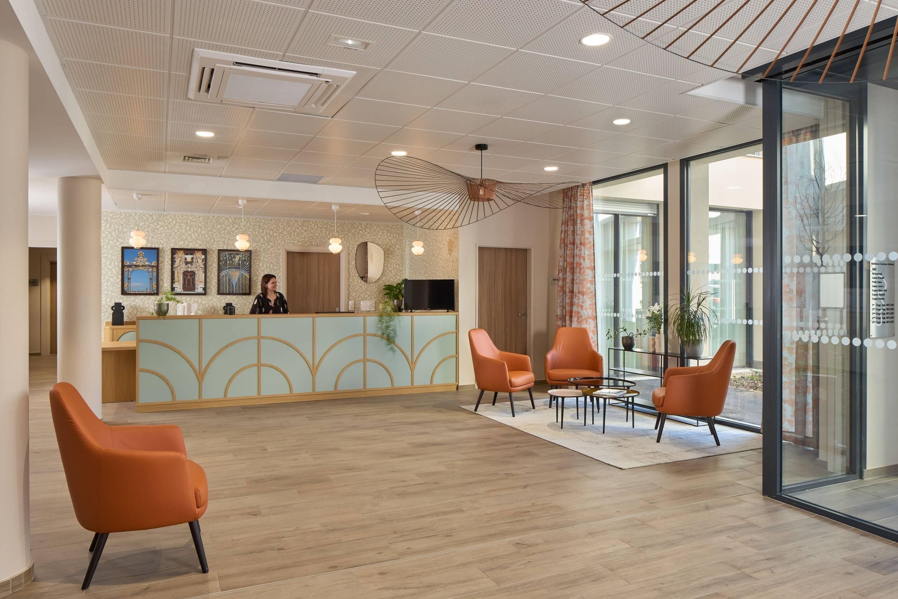 Zona de recepción con mostrador, sillas color naranja y un diseño moderno del techo.