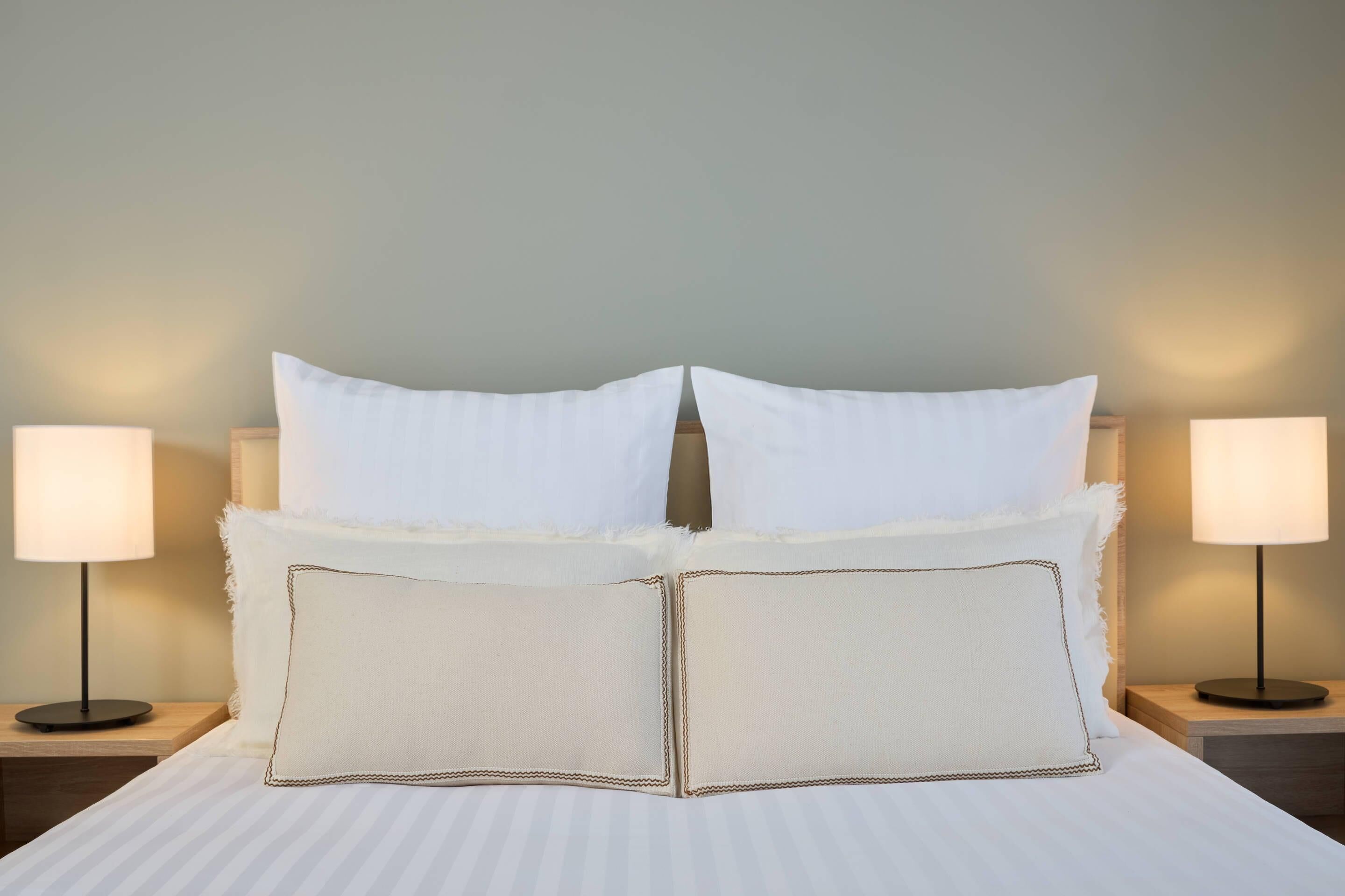 A neatly made bed with white linens and two bedside lamps on wooden nightstands.