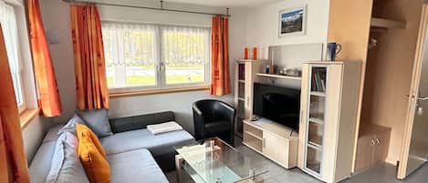 Una sala de estar moderna con un sofá, una mesa de centro de vidrio, un televisor y un aparador.