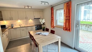 A modern kitchen with white cabinets, a dining table with chairs, and a view of a garden through a sliding glass door. - Alpi Retreat by Saas Grund (Saas Grund)