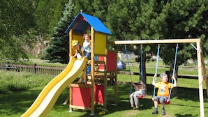 A playground with a yellow slide, a swing set, and a wooden playhouse. - Alpi Retreat by Saas Grund (Saas Grund)