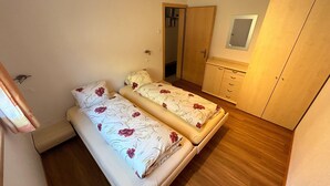 A small bedroom with two beds, a wooden wardrobe, a mirror, and a door. - Alpi Retreat by Saas Grund (Saas Grund)