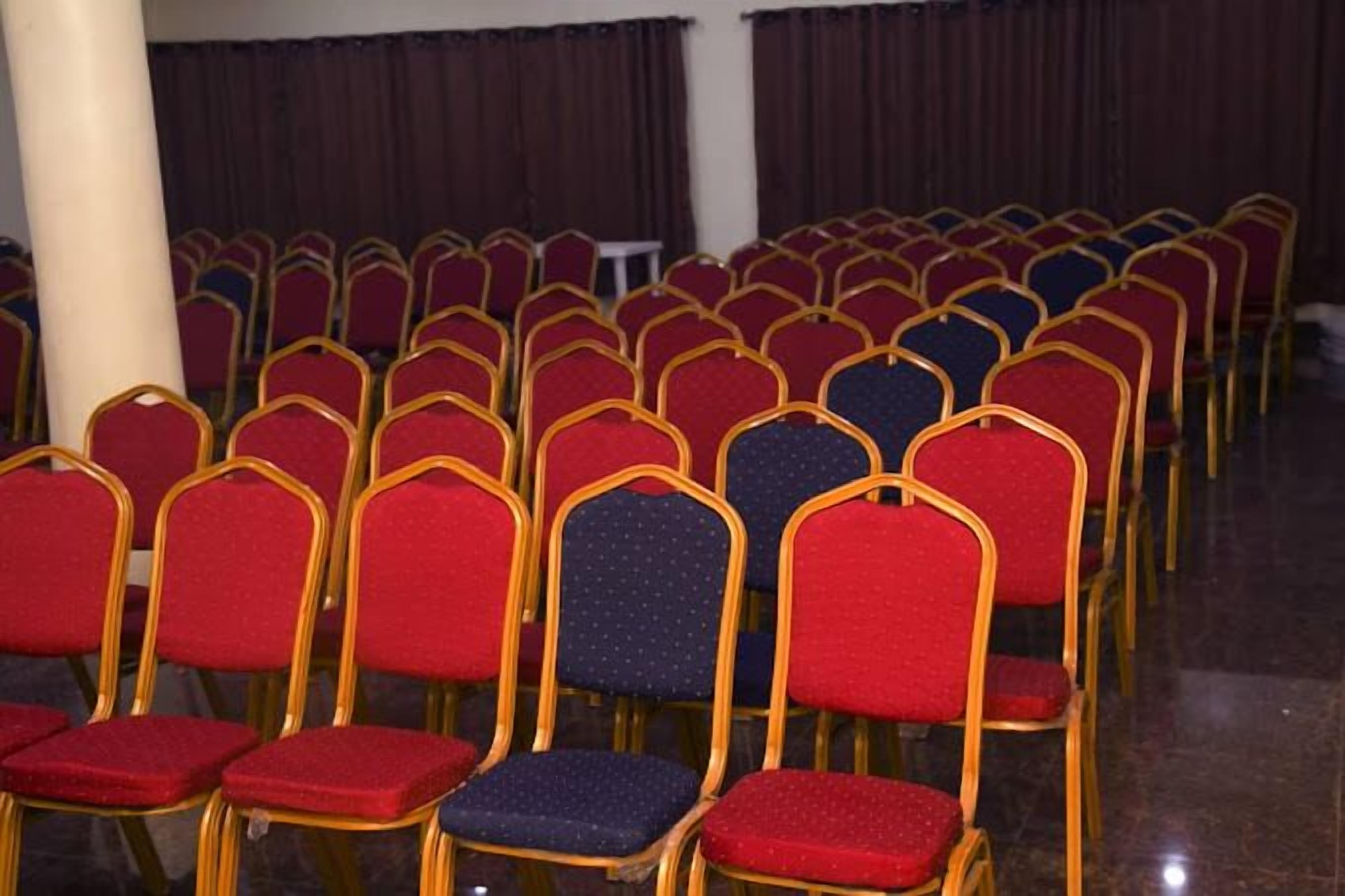 Filas de sillas rojas y azules con marcos dorados en una sala de conferencias.