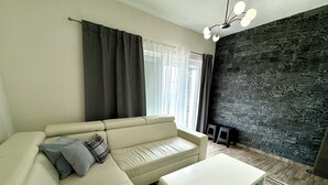 Un salon moderne avec un canapé d’angle beige, une table basse blanche et un mur d’accent en pierre sombre.