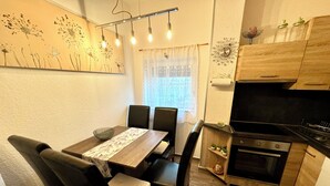 Une cuisine compacte avec un coin repas, des meubles en bois, une cuisinière noire et une fenêtre avec des rideaux.