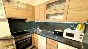 Une cuisine compacte dotée de meubles en bois, d’un four encastré, d’un lave-vaisselle, d’un four à micro-ondes et d’une bouilloire.