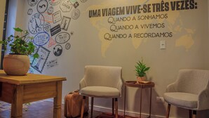A room with a wall decorated with travel stamps and a map, two chairs, a small table, and a potted plant. - Che Hermano Suítes (Foz do Iguaçu)