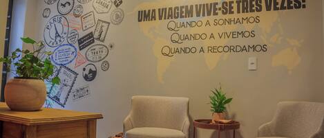 A room with a wall decorated with travel stamps and a map, two chairs, a small table, and a potted plant.