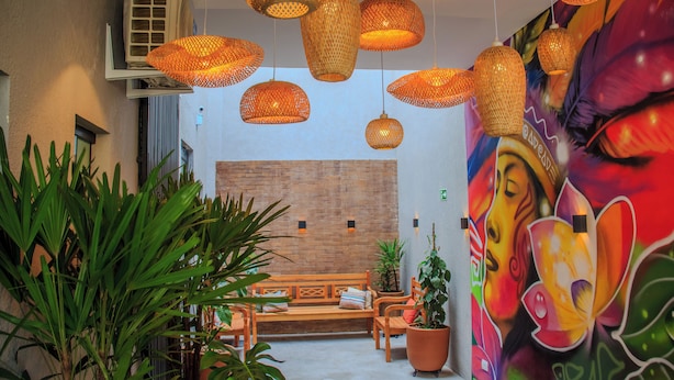 A lobby with wicker pendant lighting, a mural, a wooden bench, and potted plants. - Che Hermano Suítes (Foz do Iguaçu)
