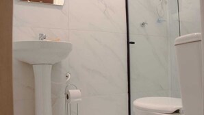 A bathroom with a white sink, toilet, and glass shower enclosure. - Che Hermano Suítes (Foz do Iguaçu)