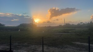 A rural landscape with a sunset, a fenced area, and grazing animals.
