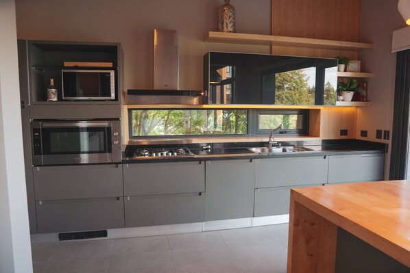 A modern kitchen with built-in appliances, a window with a view of trees, and a wooden table.