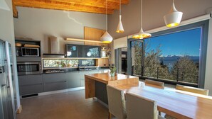 A modern kitchen with a wooden island, stainless steel appliances, and large windows offering a view of mountains. - House of Light Bariloche (San Carlos de Bariloche)