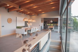 Uma cozinha moderna com uma ilha grande, uma sala de jantar com uma mesa comprida e cadeiras, e uma escadaria que leva a um andar superior.