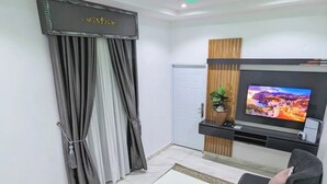 A modern living room with a white coffee table, dark sofas, a patterned rug, and a TV on the wall. - Urban Edge Comfort Apartment (Lokoja)