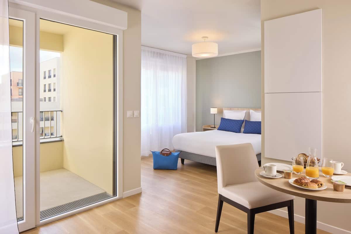 Quarto de hotel com cama, mesa com café da manhã, mala e vista para prédios.