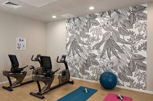 Un gimnasio con dos bicicletas estáticas, una pelota de ejercicios grande y mancuernas sobre colchonetas.