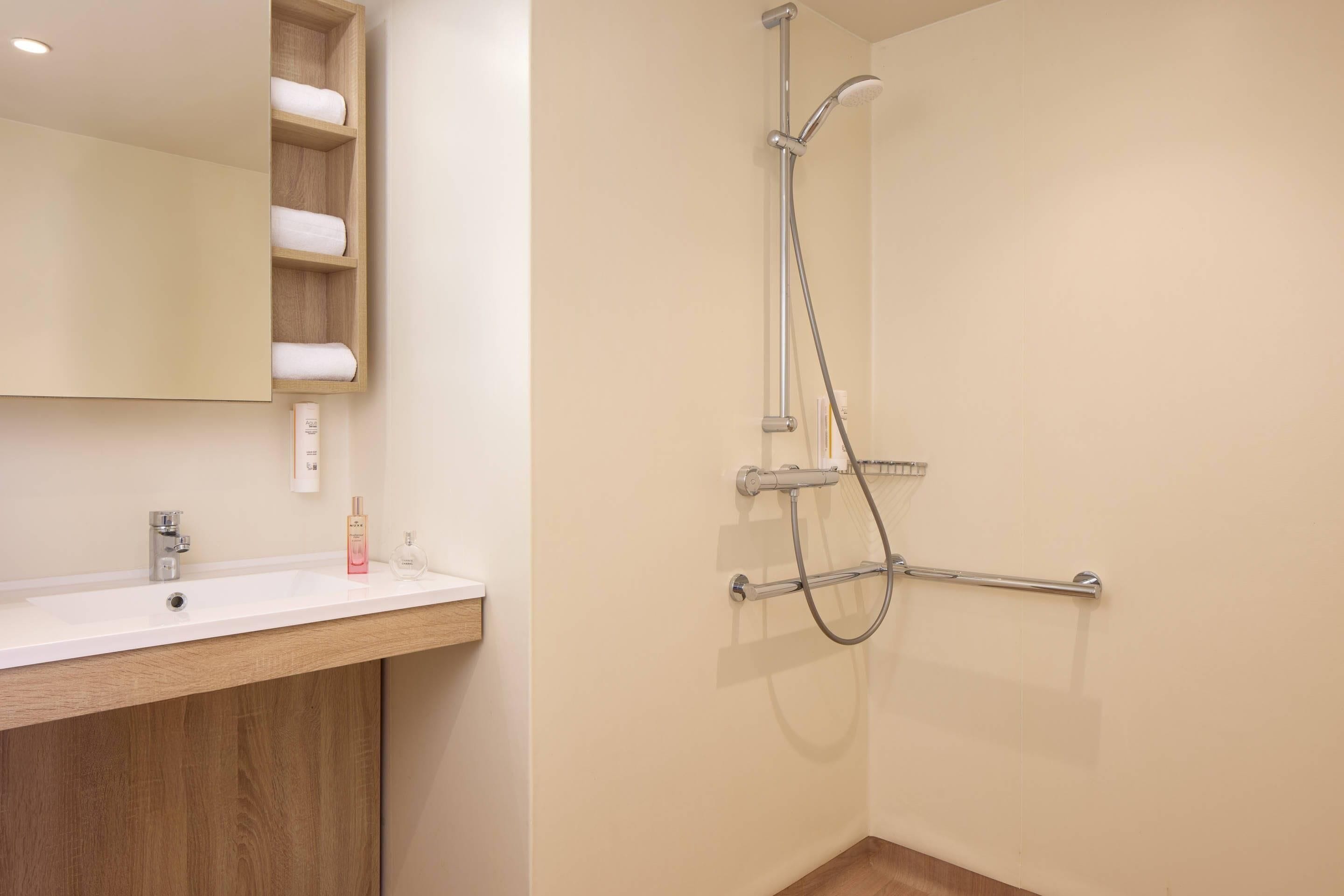 Bagno con lavandino bianco, mobile contenitore in legno, specchio, doccia con soffione manuale e portasci.
