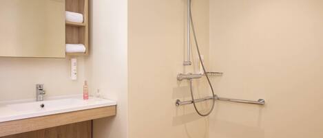 A bathroom with a white sink, wooden vanity, a mirror, a shower with a handheld showerhead, and a towel rack.