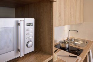 Una cocina compacta con microondas, estufa, pileta y tabla de cortar.